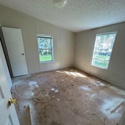Empty room under renovation with concrete floor, windows, white door, and electrical wiring